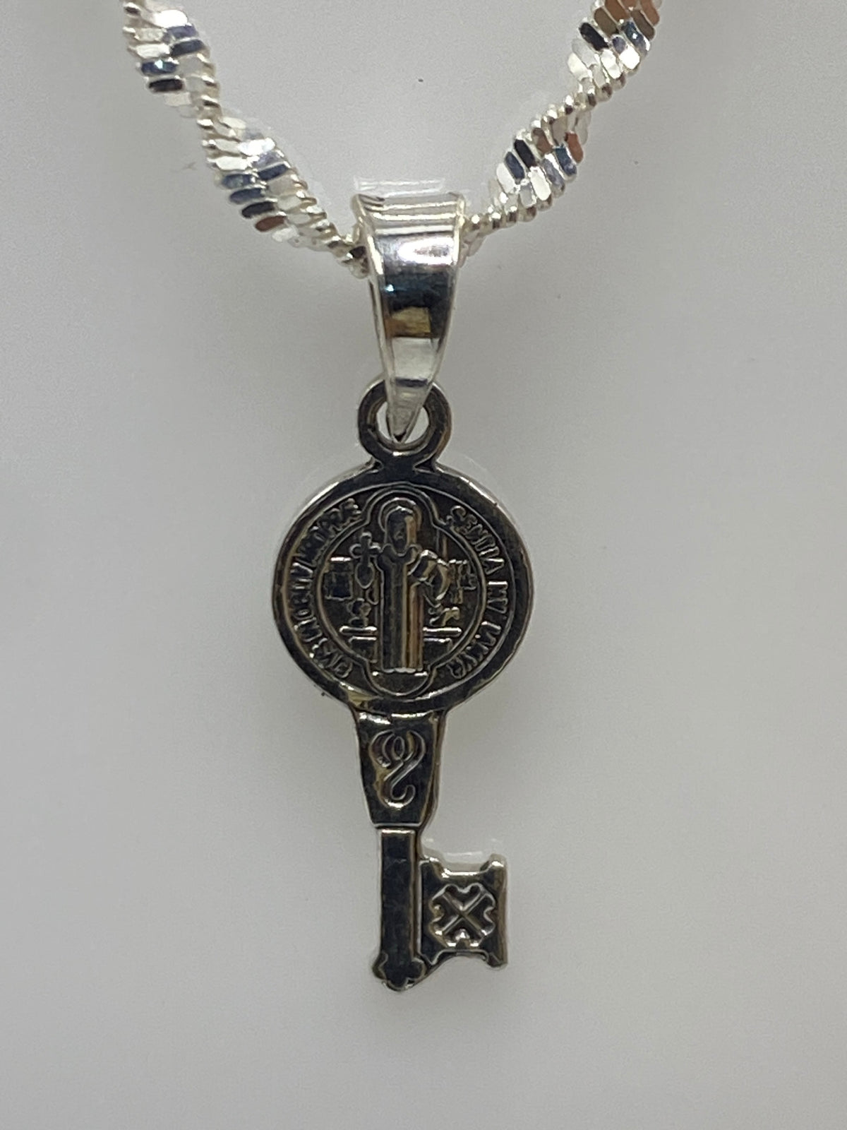 Dije llave de San Benito en plata 925 repujada, medida 2 cm, con cadena plateada