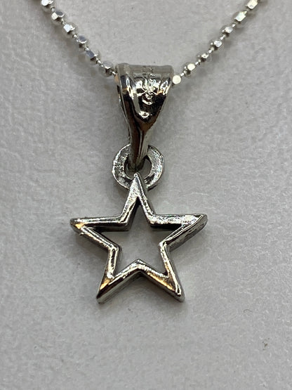Dije de plata en forma de estrella abierta, calado, colgando de una cadena de bolitas