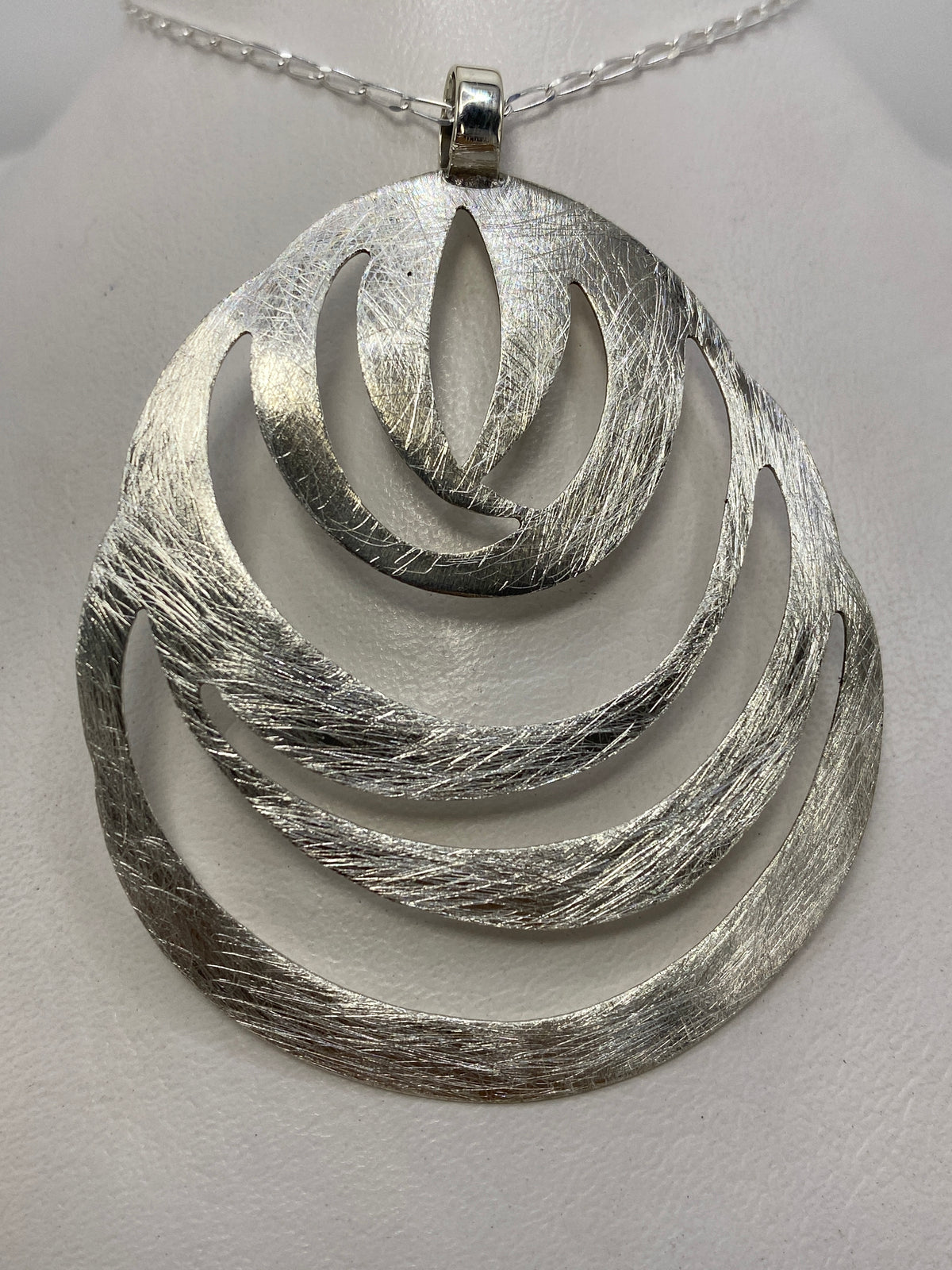 Dije de plata de 6.2 cm con volúmenes geométricos anidados, texturizado, colgado de una cadena clara