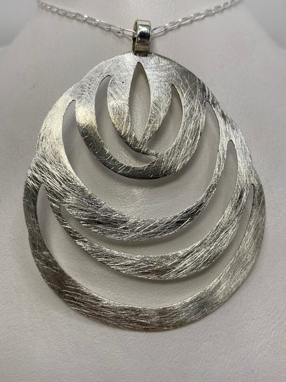 Dije de plata de 6.2 cm con volúmenes geométricos anidados, texturizado, colgado de una cadena clara