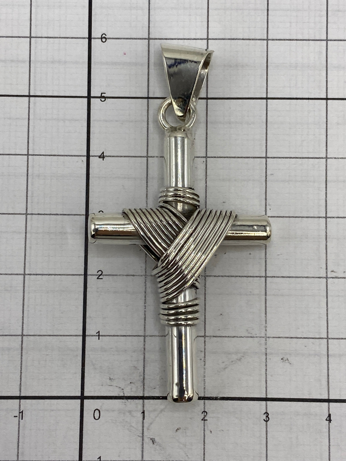 Dije cruz de plata sobre fondo neutro con escala en centímetros
