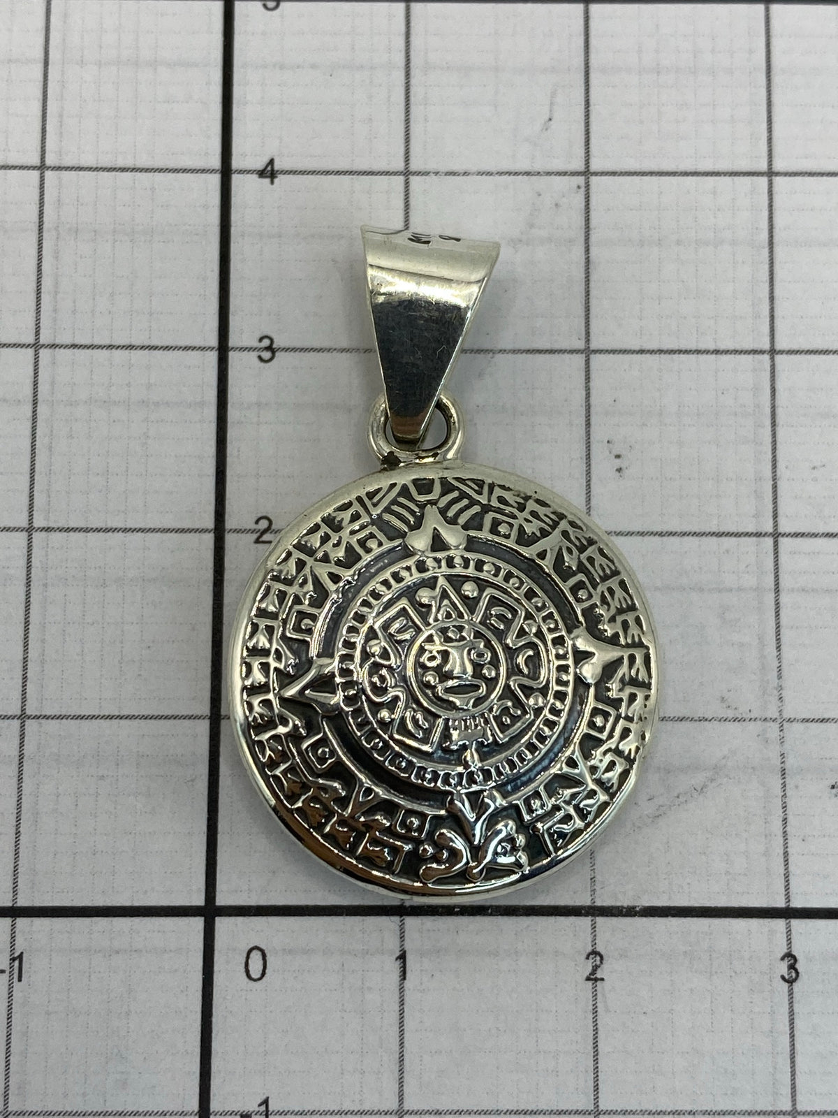Dije calendario azteca en la mano mostrando su tamaño de 3.5 cm de diámetro
