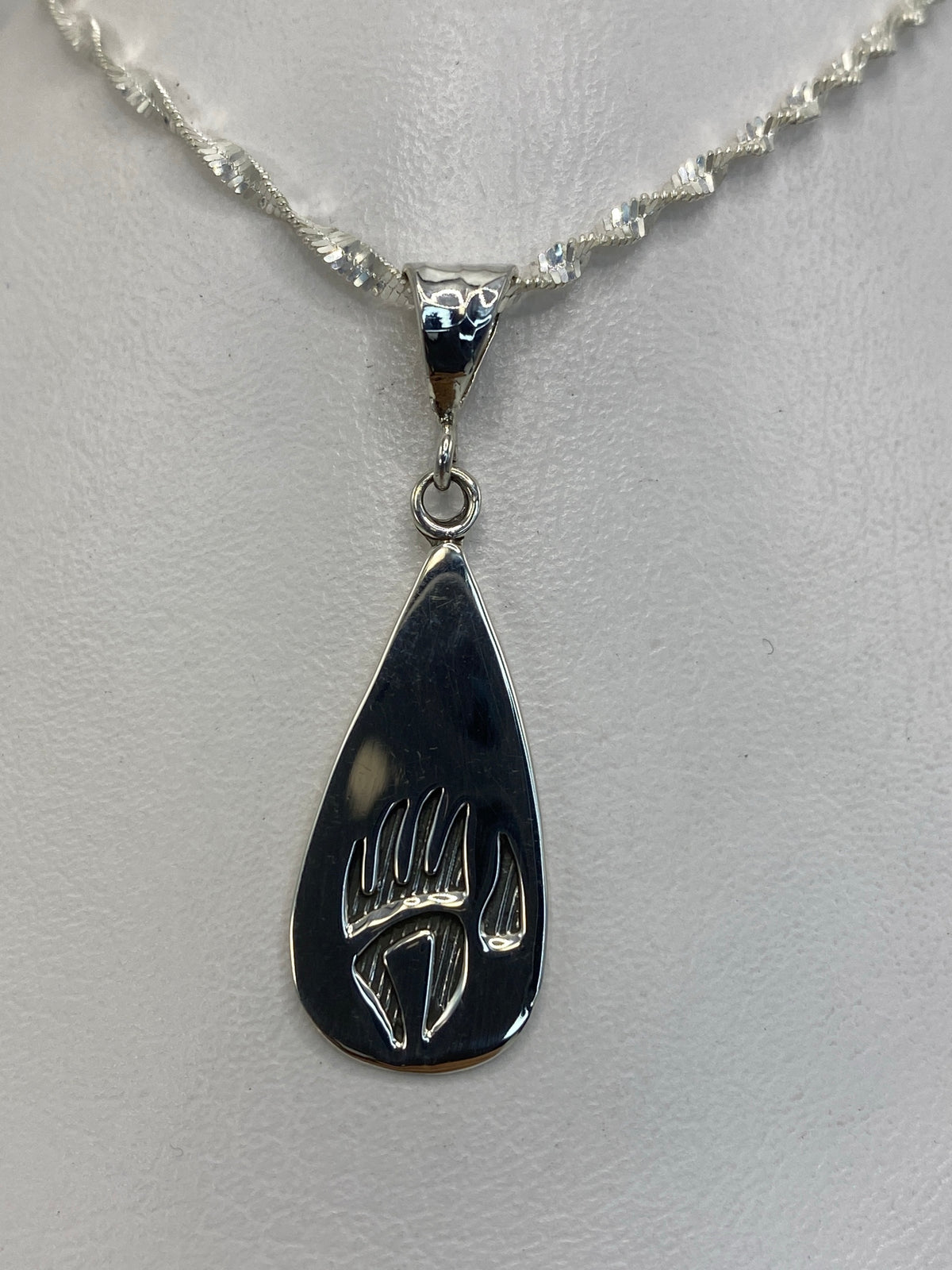 Dije de plata garra de oso colgante sobre fondo blanco, vista frontal del diseño grabado