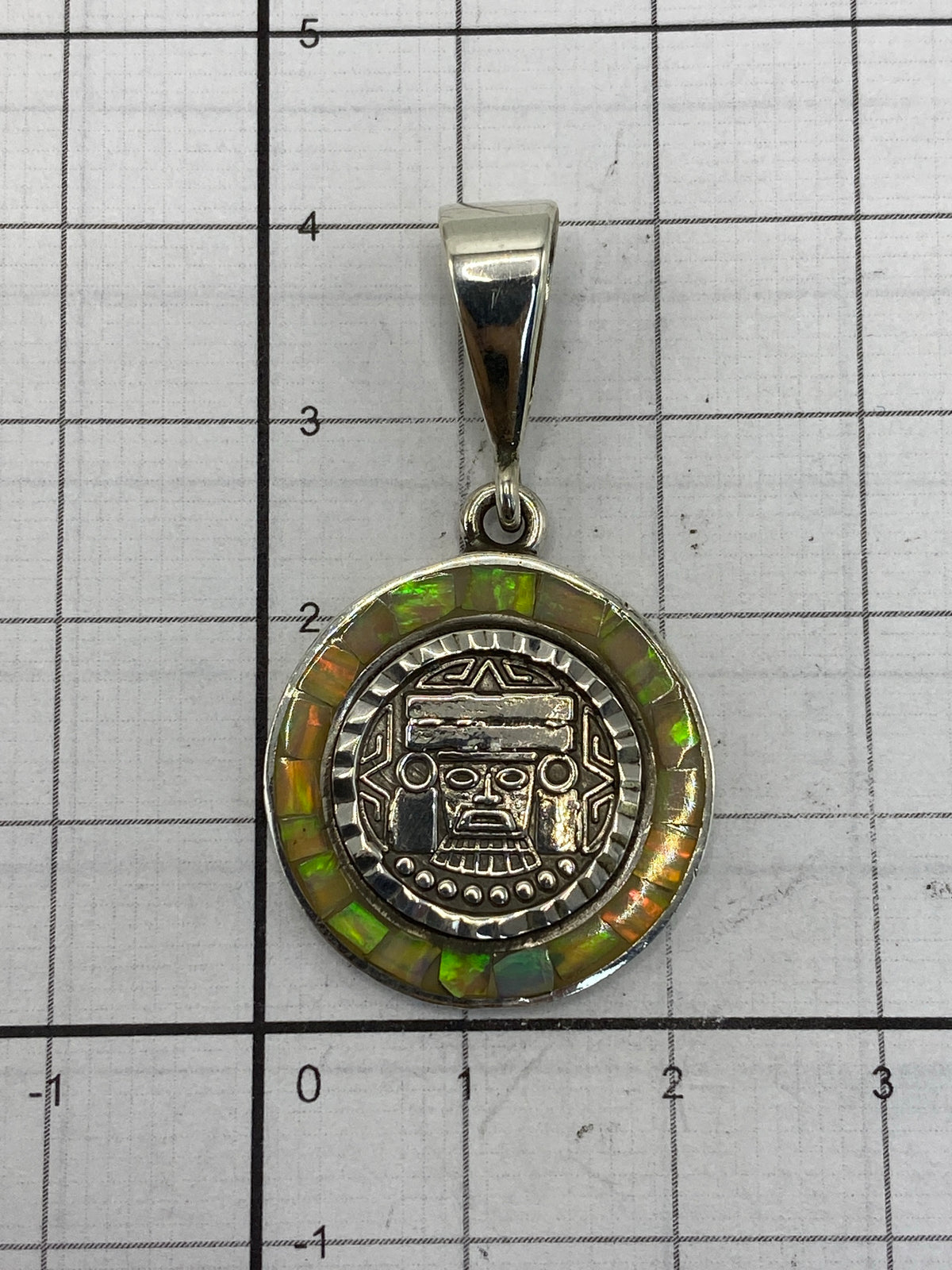 Dije de máscara azteca colgando sobre fondo blanco, comparación de tamaño real 4 cm