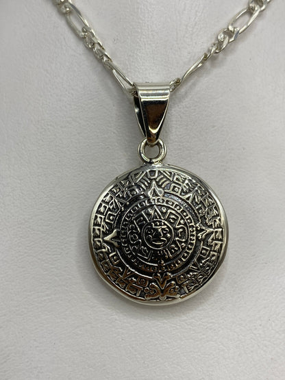 Dije de plata con diseño del calendario azteca prehispánico, colgando de una cadena plateada
