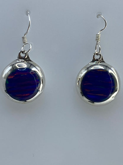 Par de aretes de plata 925 con ópalo de fuego azul, colgando sobre fondo gris