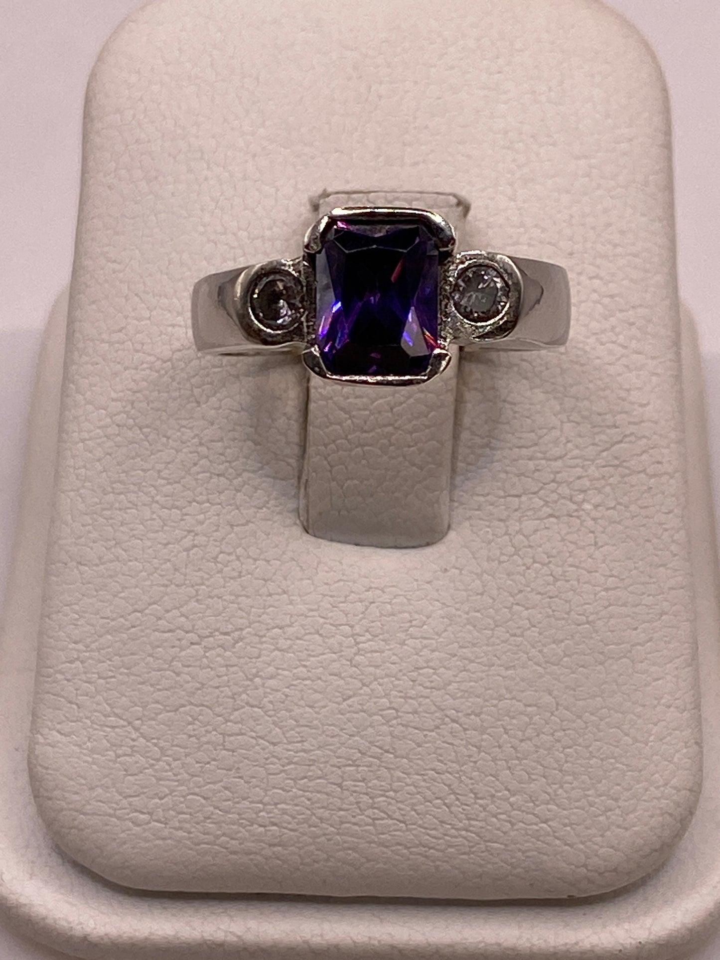 Anillo solitario de plata con circonia púrpura en la mano de una mujer, frente a fondo blanco