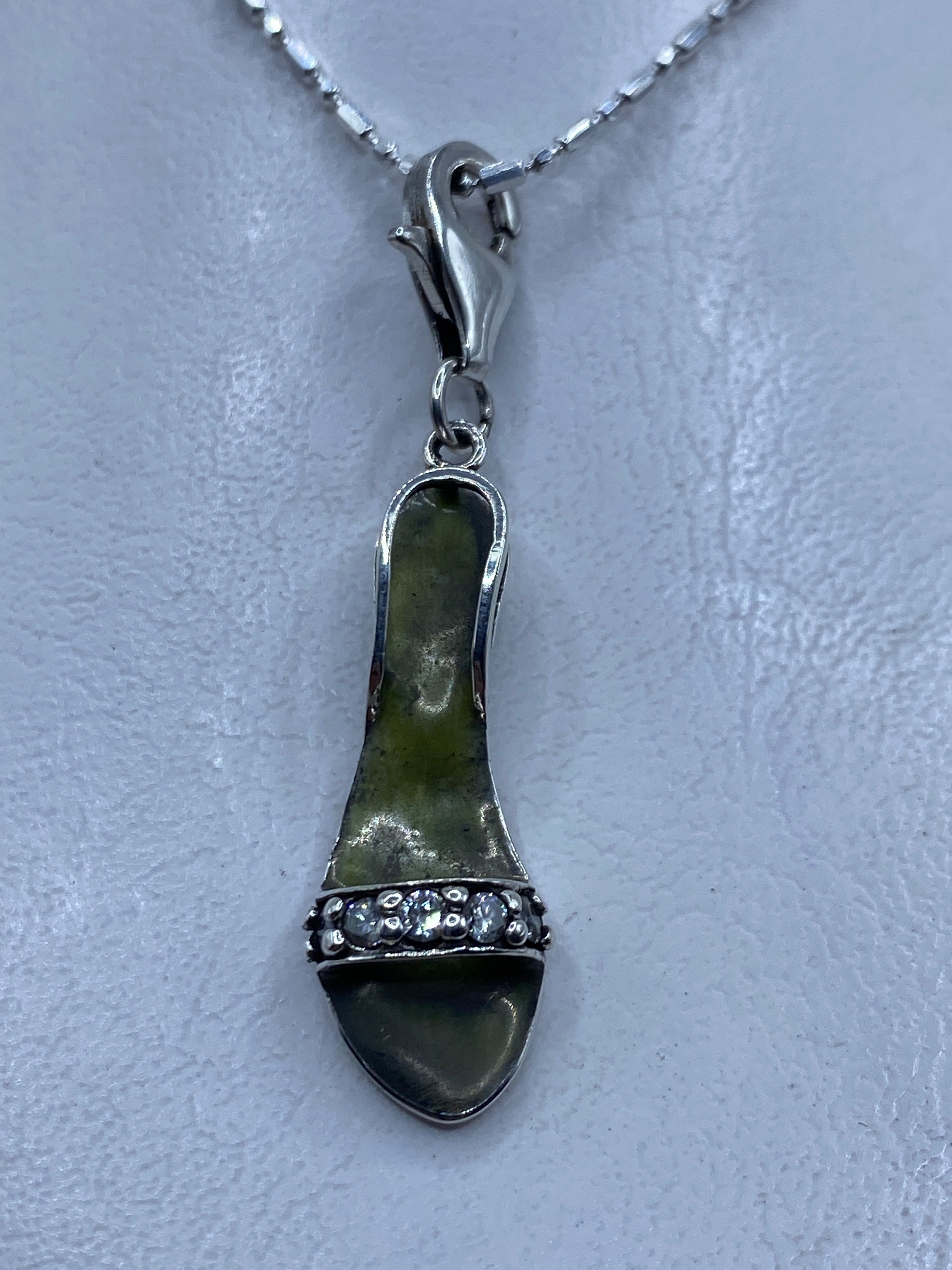 Dije de plata con circonia verde olivo de 5 cm colgando de la mano