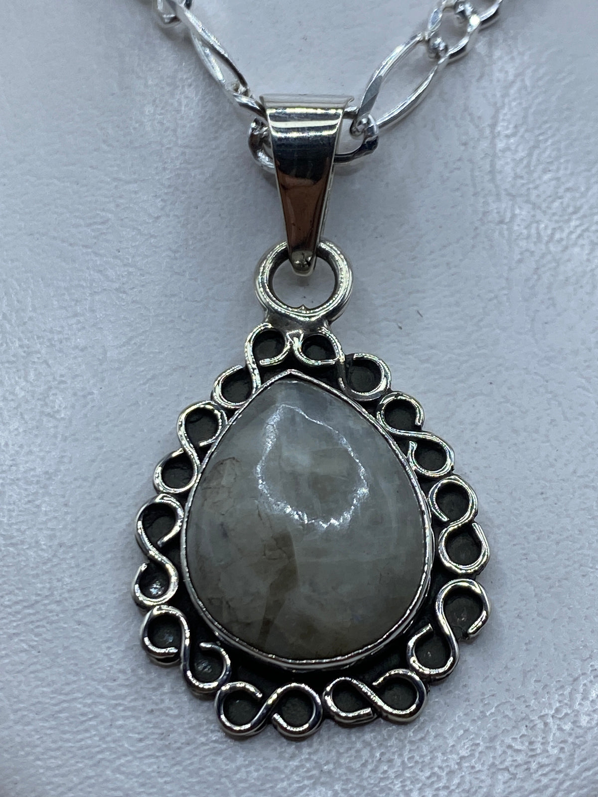 Dije de plata con piedra blanca engastada en marco floral, colgado en cadena plateada