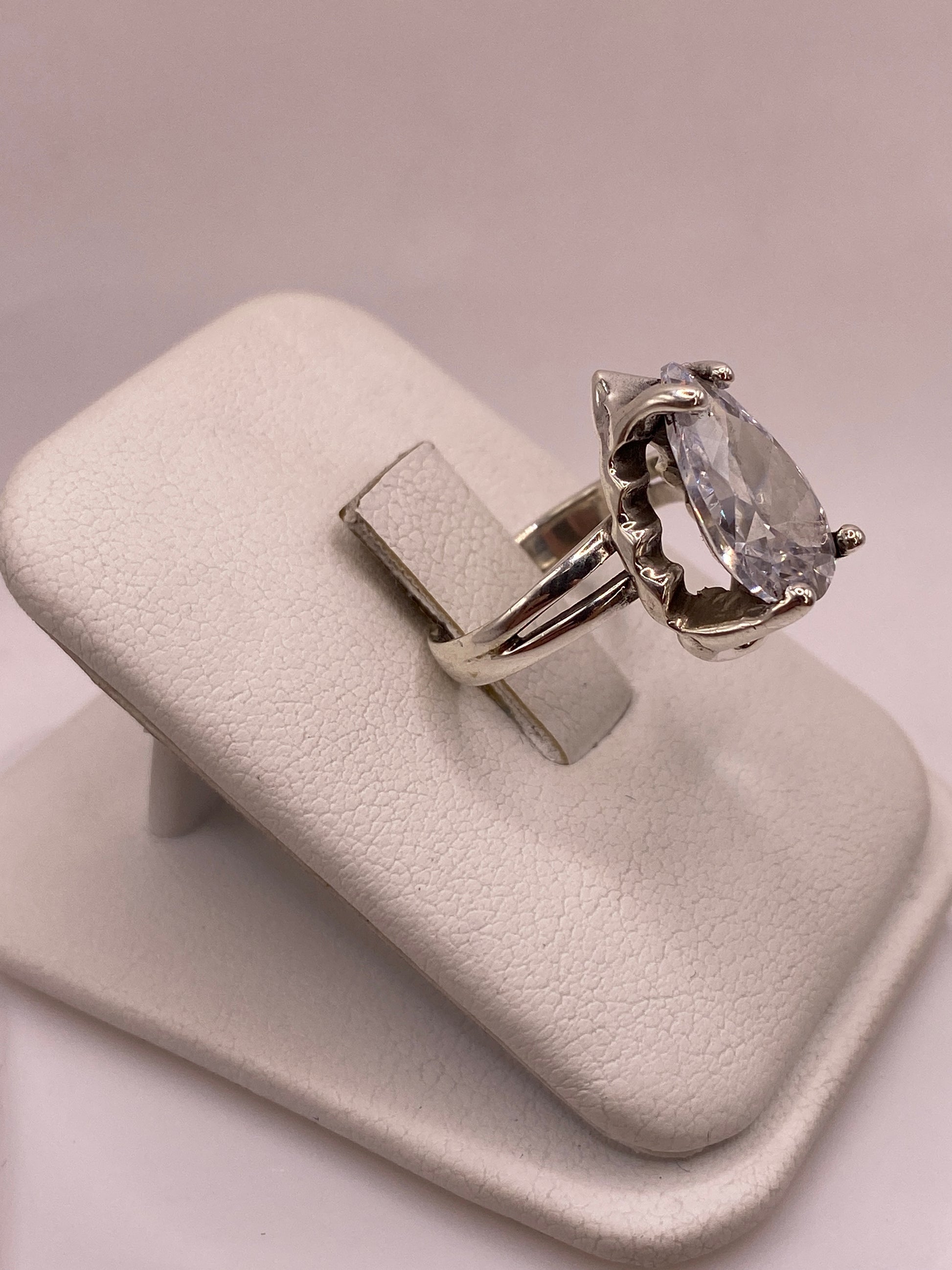 Vista lateral del anillo solitario en plata con montura calada y circonia pera sobre soporte blanco