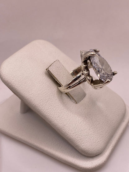 Vista lateral del anillo solitario en plata con montura calada y circonia pera sobre soporte blanco