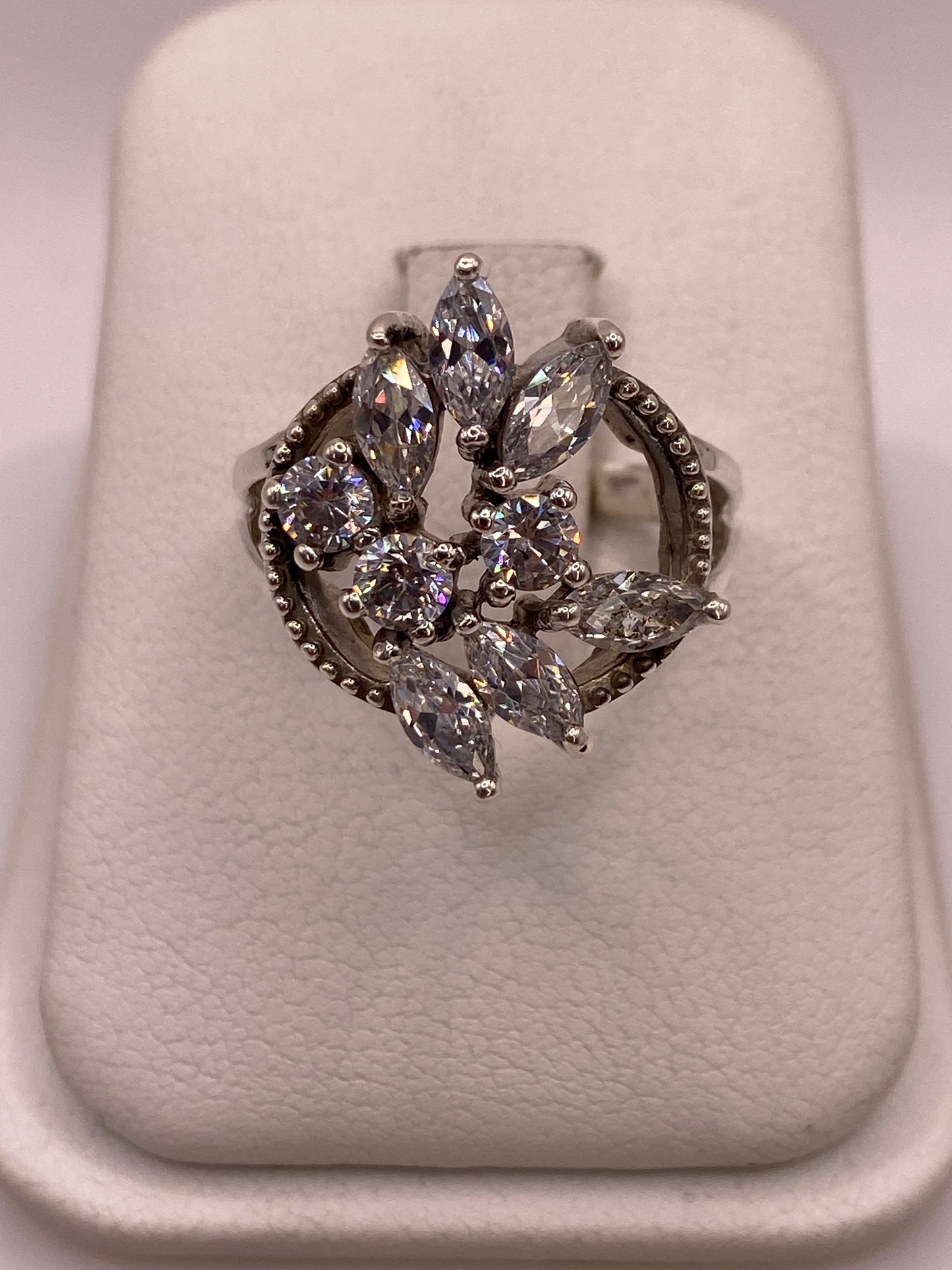 Anillo de plata .925 con circonias blancas en corte marquesa y redondo, diseño floral tipo coctel, vista frontal sobre exhibidor