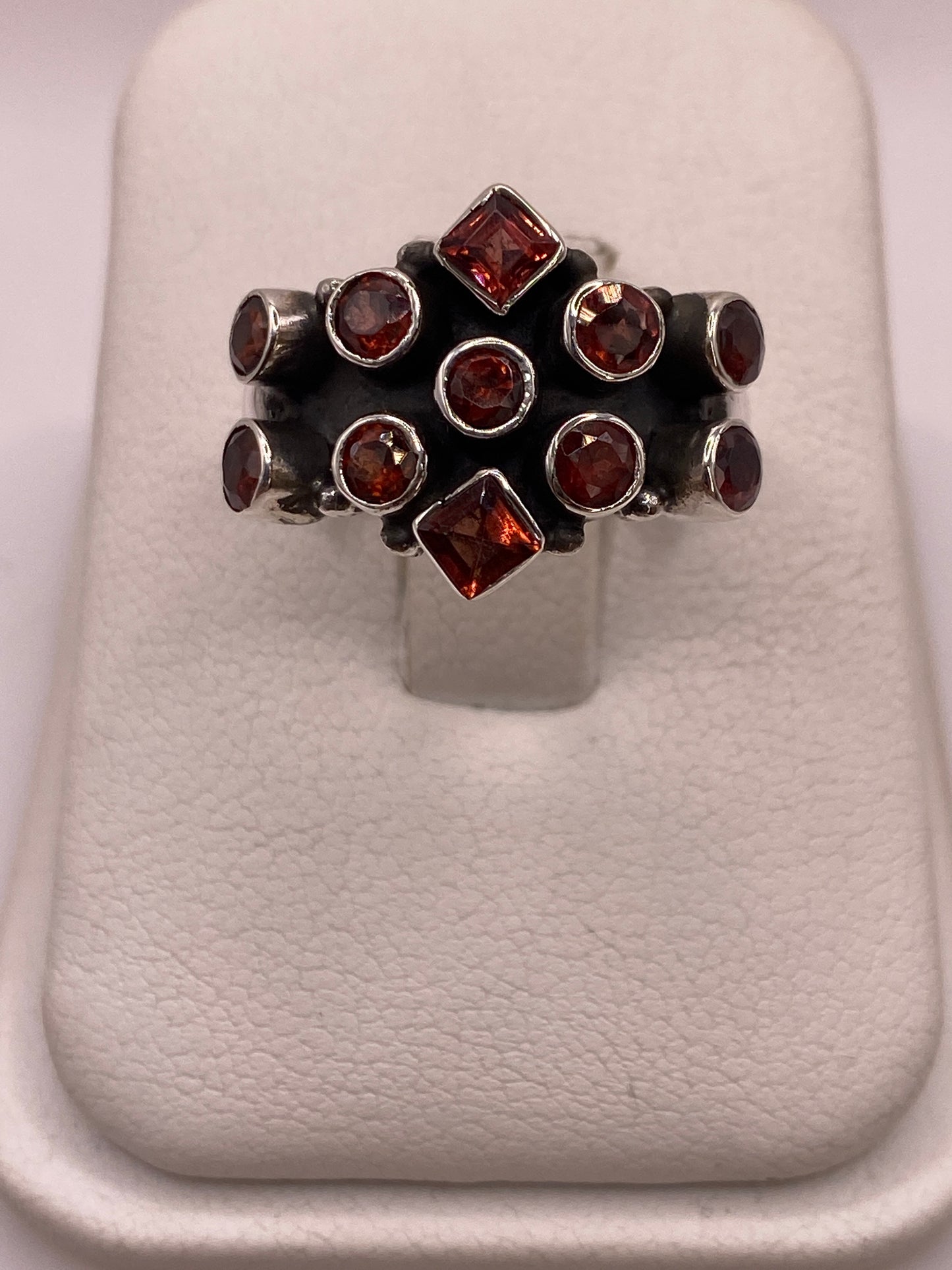 Anillo de plata .925 con racimo de 11 circonias rojo granate, estilo coctel vintage, vista frontal sobre display blanco