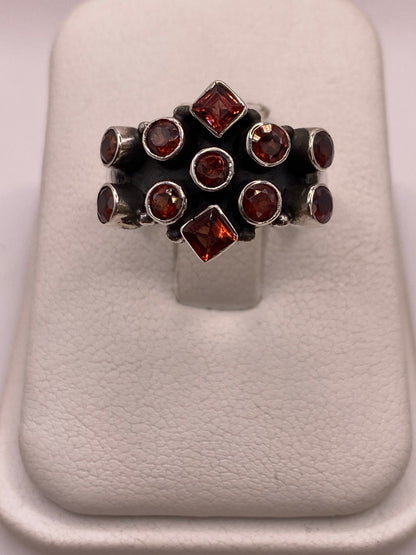 Anillo de plata .925 con racimo de 11 circonias rojo granate, estilo coctel vintage, vista frontal sobre display blanco