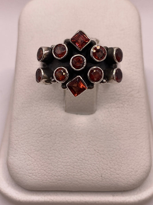 Anillo de plata .925 con racimo de 11 circonias rojo granate, estilo coctel vintage, vista frontal sobre display blanco