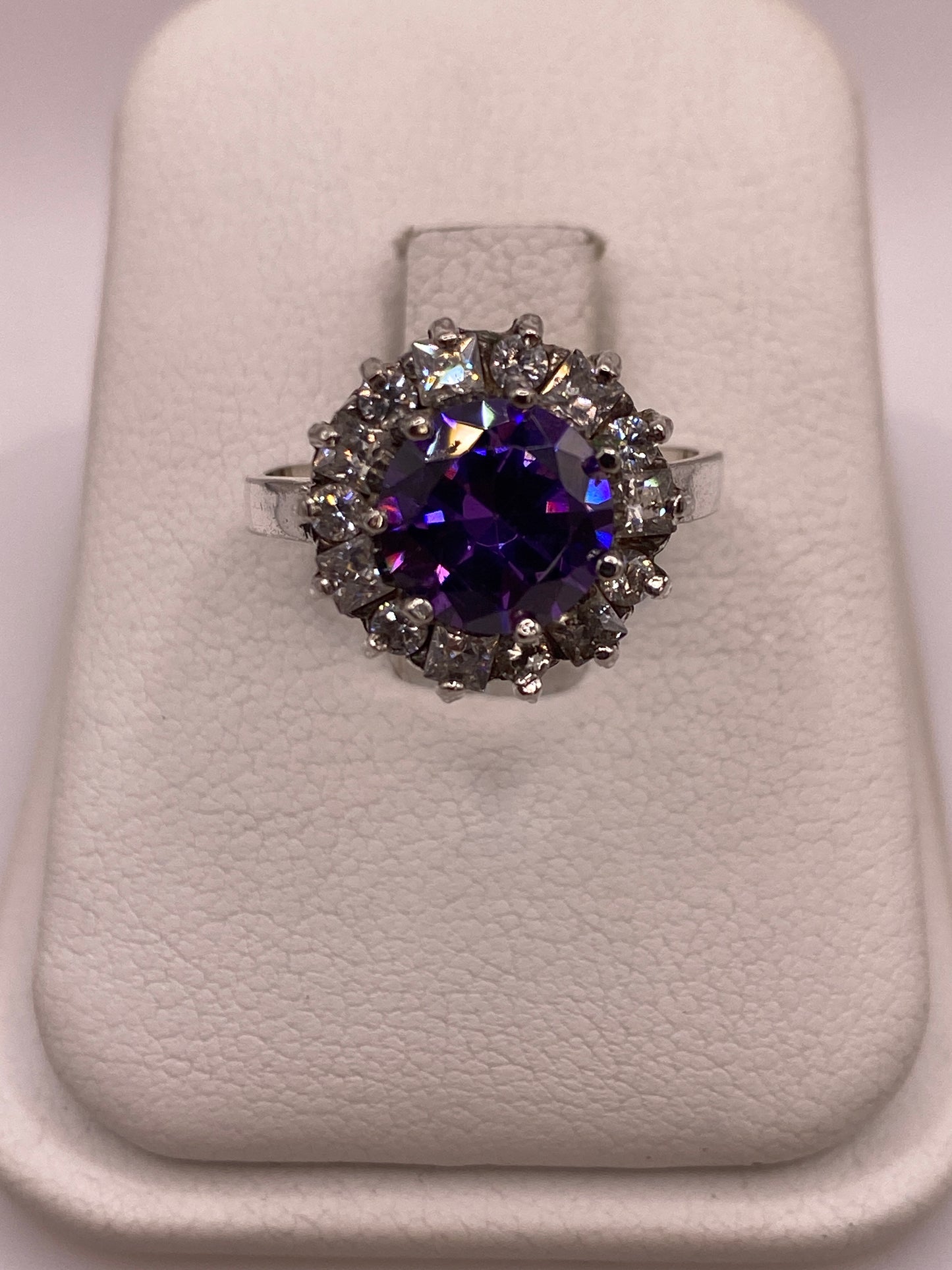 Anillo de plata .925 con circonia morada central y halo de circonias blancas sobre exhibidor blanco
