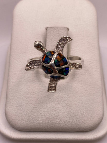 Anillo solitario de plata .950 con ópalo de fuego multicolor sobre dedo de mujer con uñas rosa