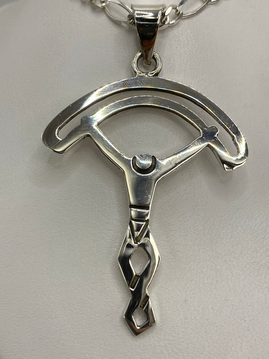 Dije de plata calado en forma de dos arcos simétricos, 6.7 cm de largo, sobre fondo blanco