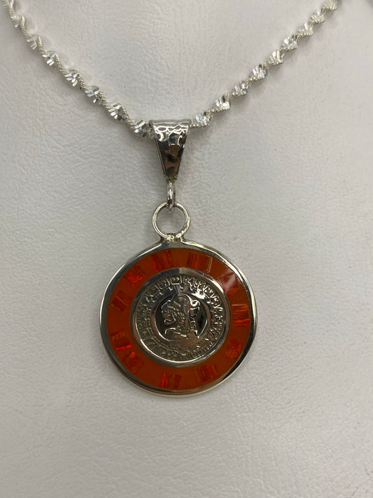 Vista frontal del dije de plata: moneda prehispánica rodeada de ópalo naranja
