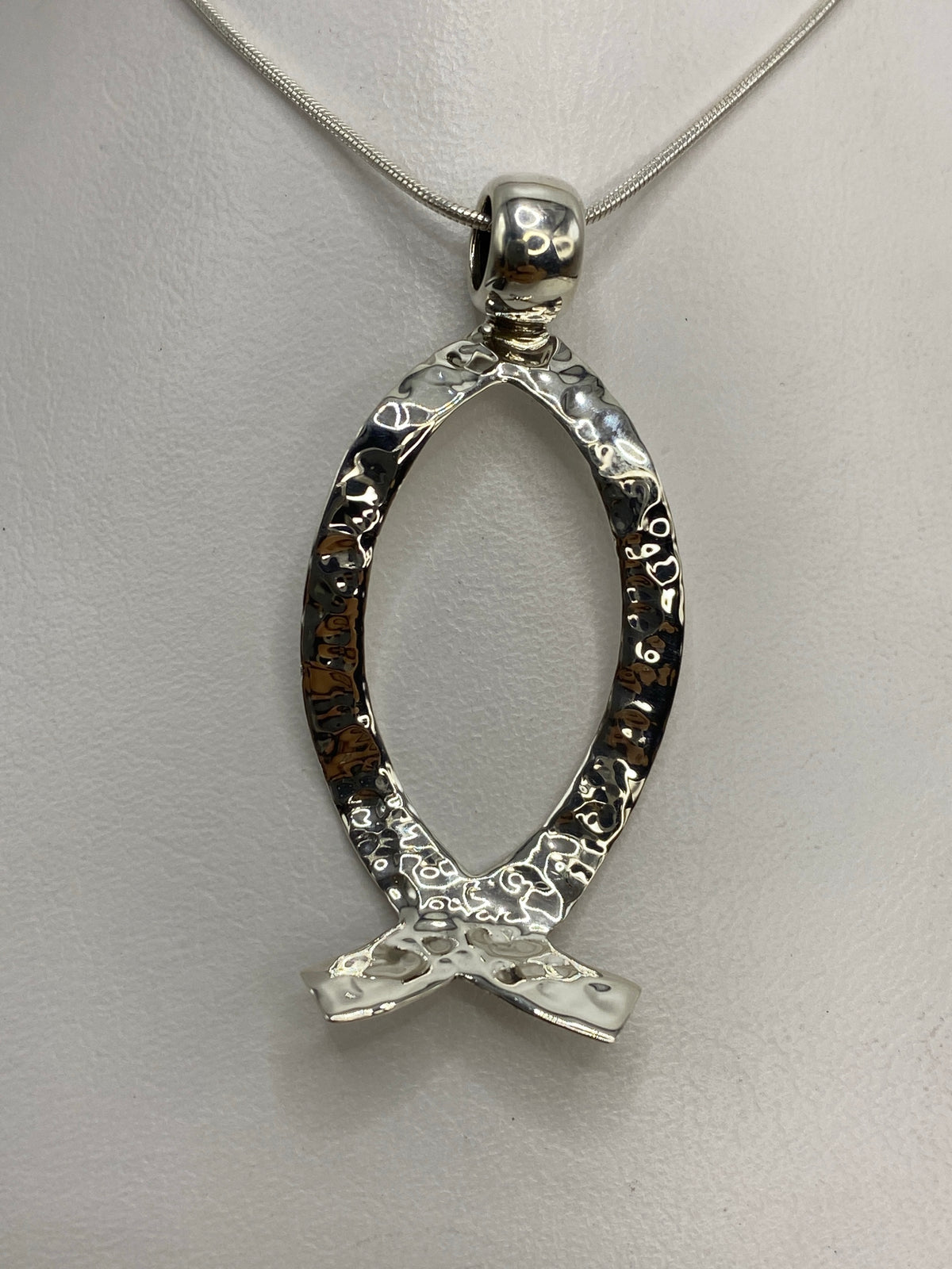 Dije de plata 925 en repujado con diseño de sello prehispánico, colgando de una cadena plateada