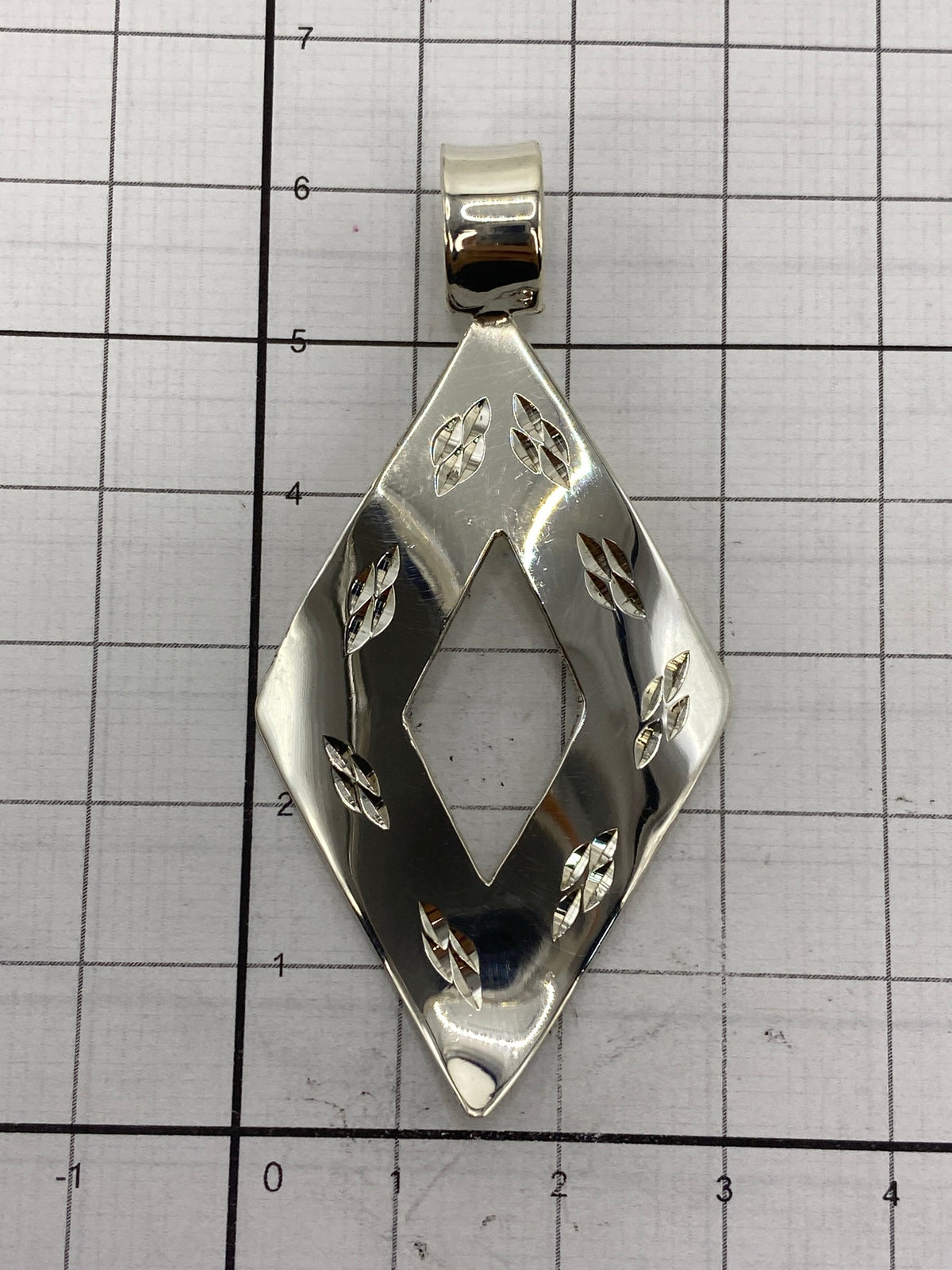 El dije de plata sobre una regla mostrando los 6 cm de largo y 3 cm de ancho