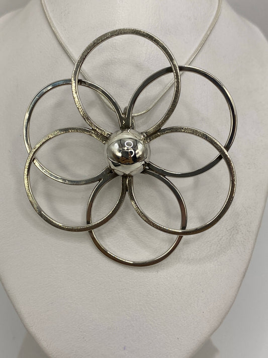 Dije floral de plata 925 con cinco pétalos en diseño geométrico, puesto sobre pecho