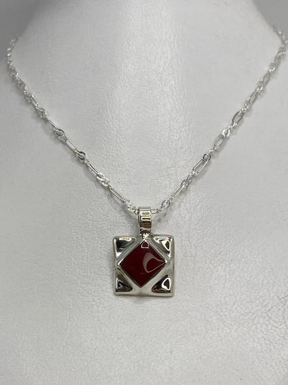 Detalle del dije compacto mostrando el engaste de piedra roja a mano