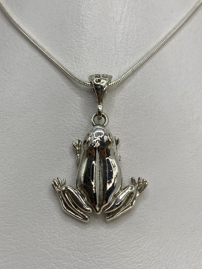 Dije de plata repujado en forma de sapo, vista frontal, colgante sobre fondo blanco