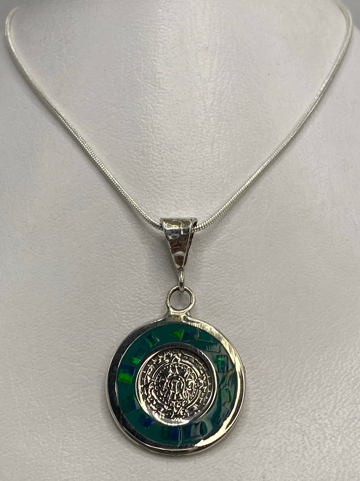 Detalle del ópalo de fuego multicolor rodeando la moneda prehispánica grabada en plata