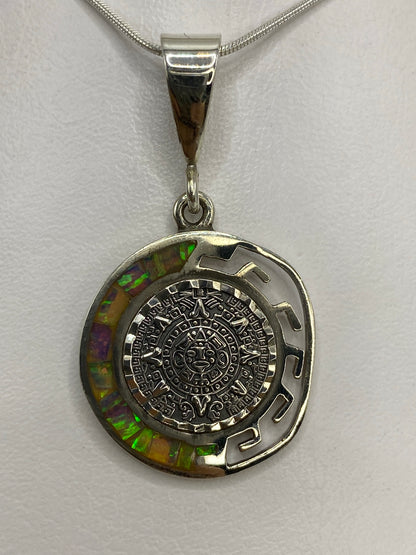 Dije del Calendario Azteca en plata 950 con ópalo de fuego multicolor colgando de una cadena plateada
