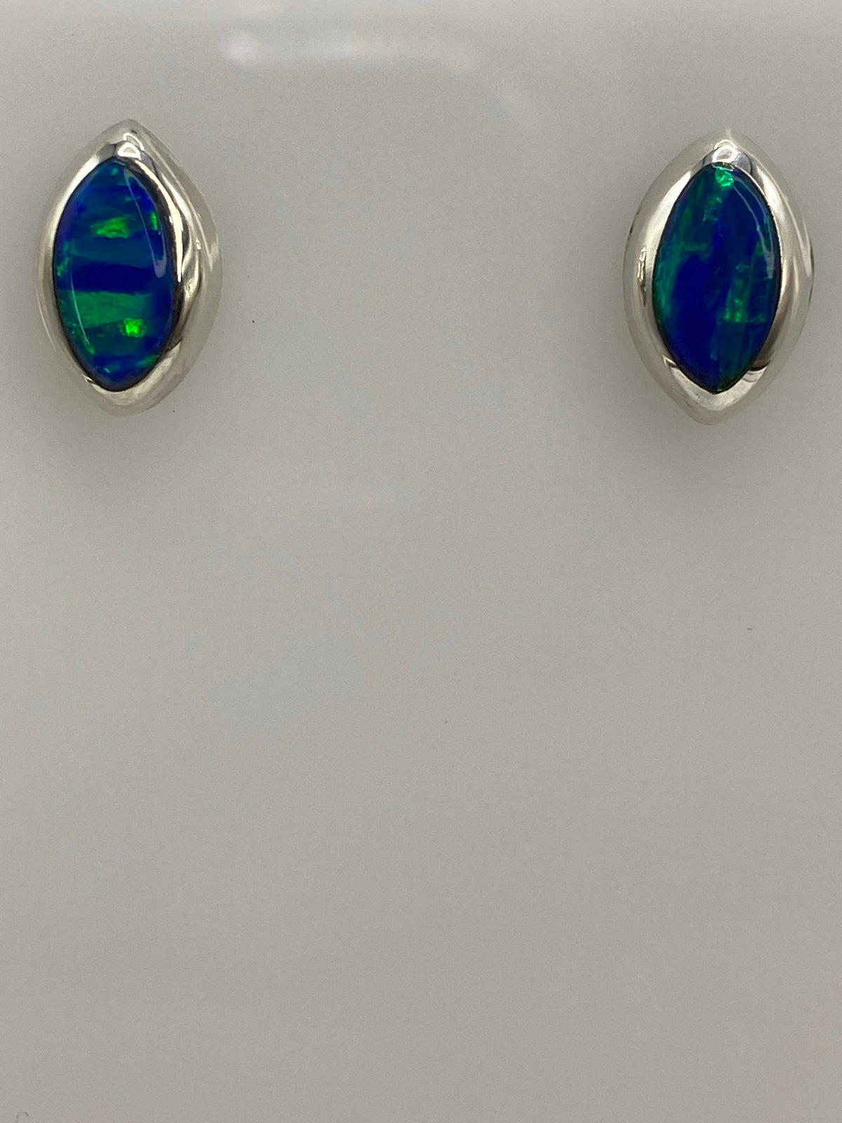 Aretes de ópalo de fuego sobre paño gris, mostrando el color azul intenso