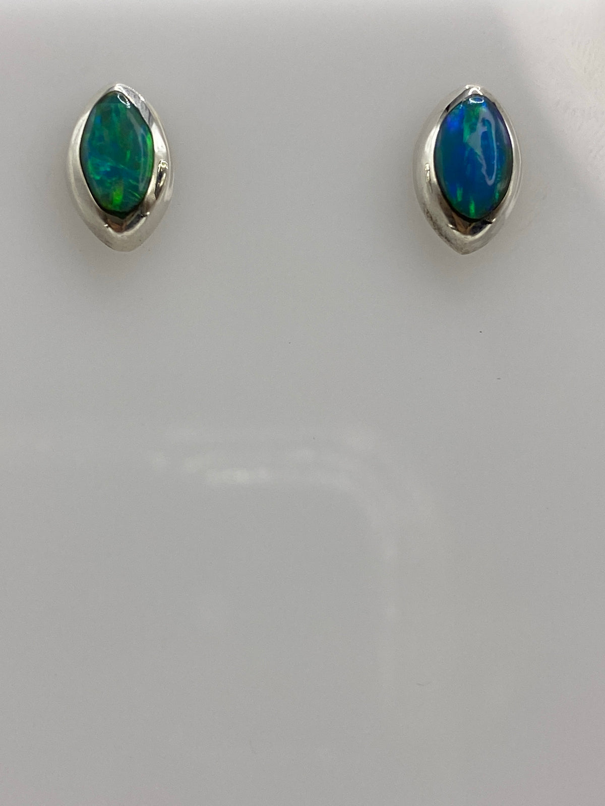 Detalle frontal de los aretes mostrando el brillo azul del ópalo de fuego