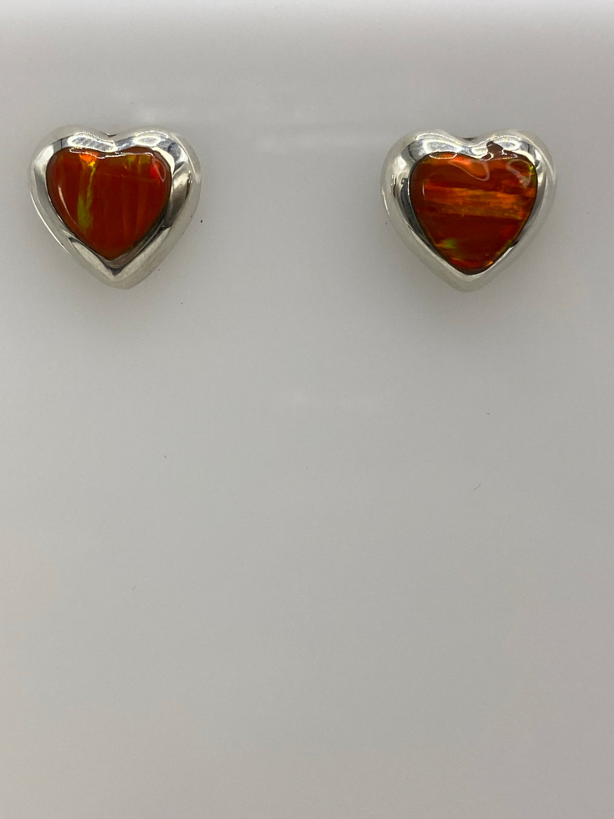 Par de aretes de plata con ópalo de fuego naranja engastado, frente a regla de centímetros