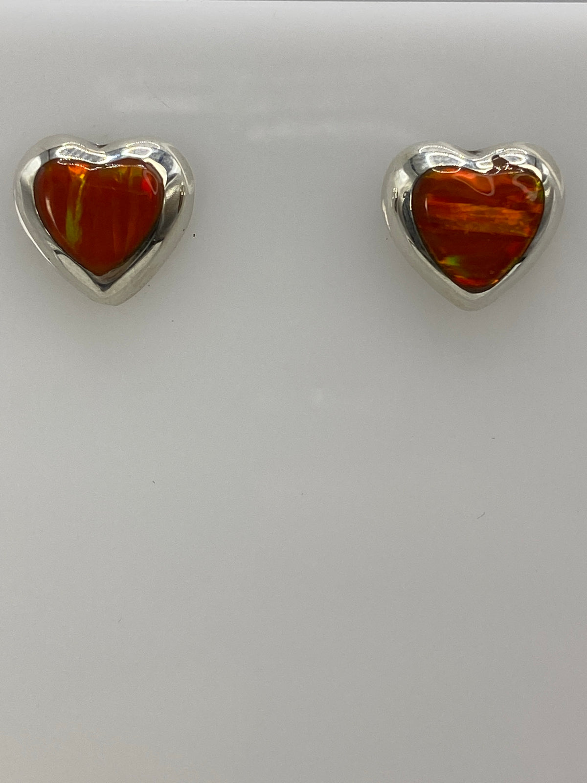 Detalle de los aretes sobre fondo gris, mostrando el fuego naranja de la piedra