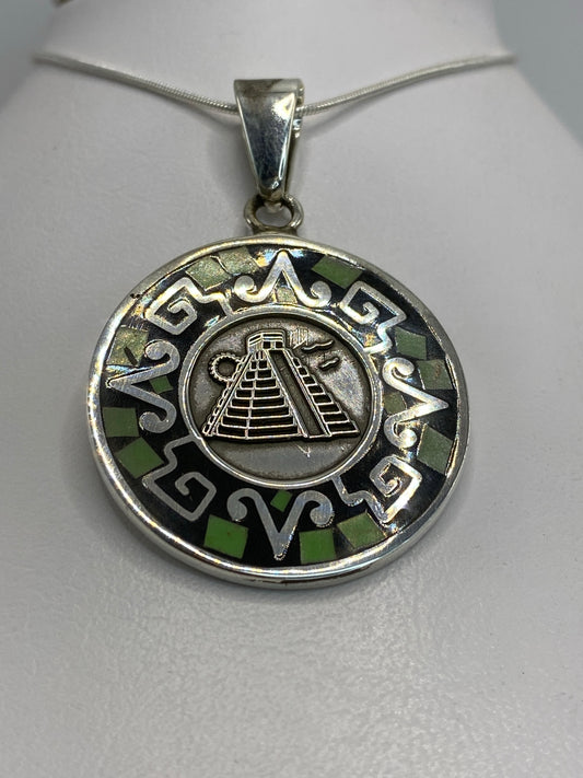 Detalle frontal del dije mostrando la pirámide de Chichén Itzá y motivos prehispánicos grabados