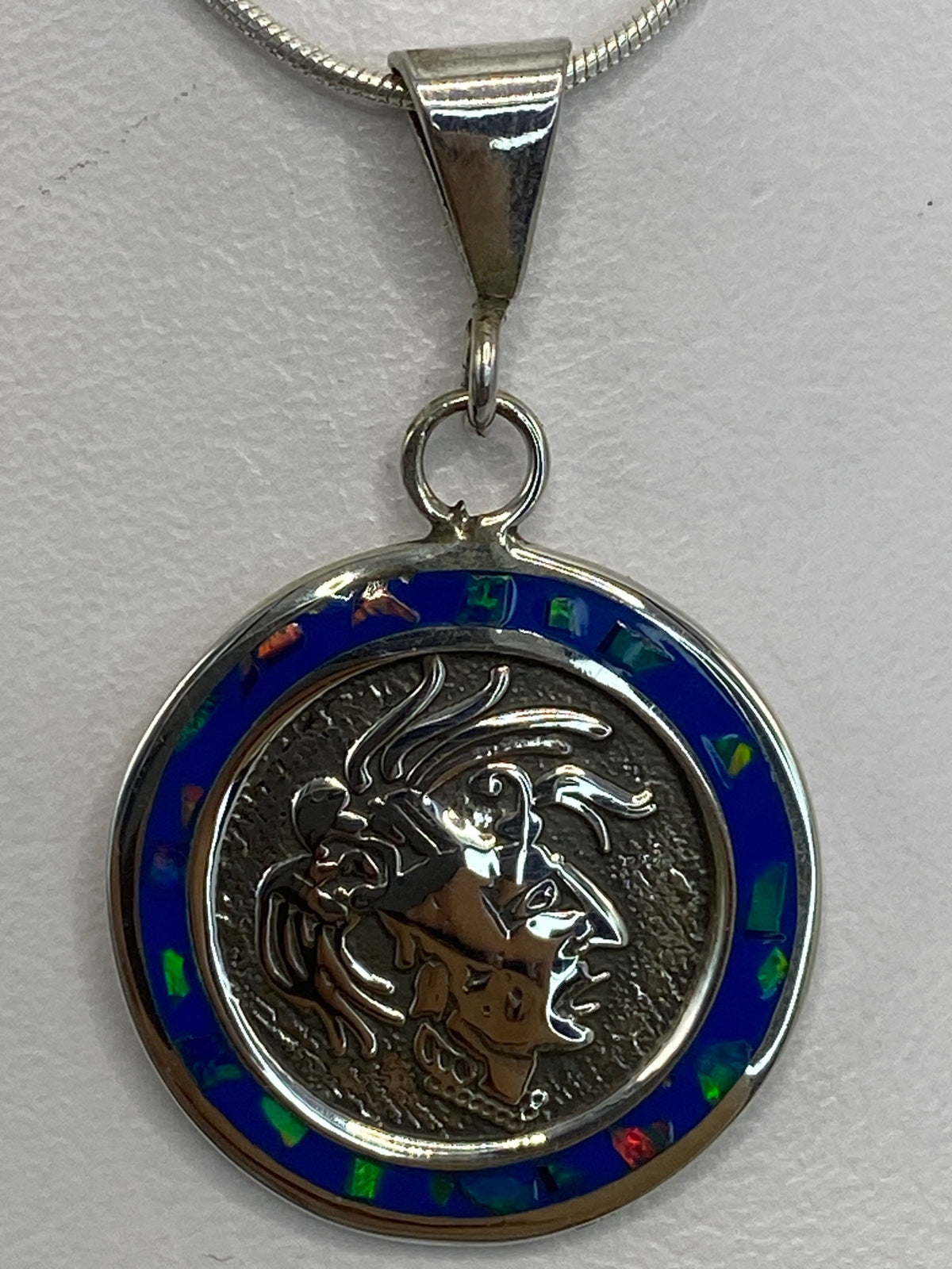 Dije de plata prehispánico con ópalo de fuego multicolor colgando de cadena, vista frontal