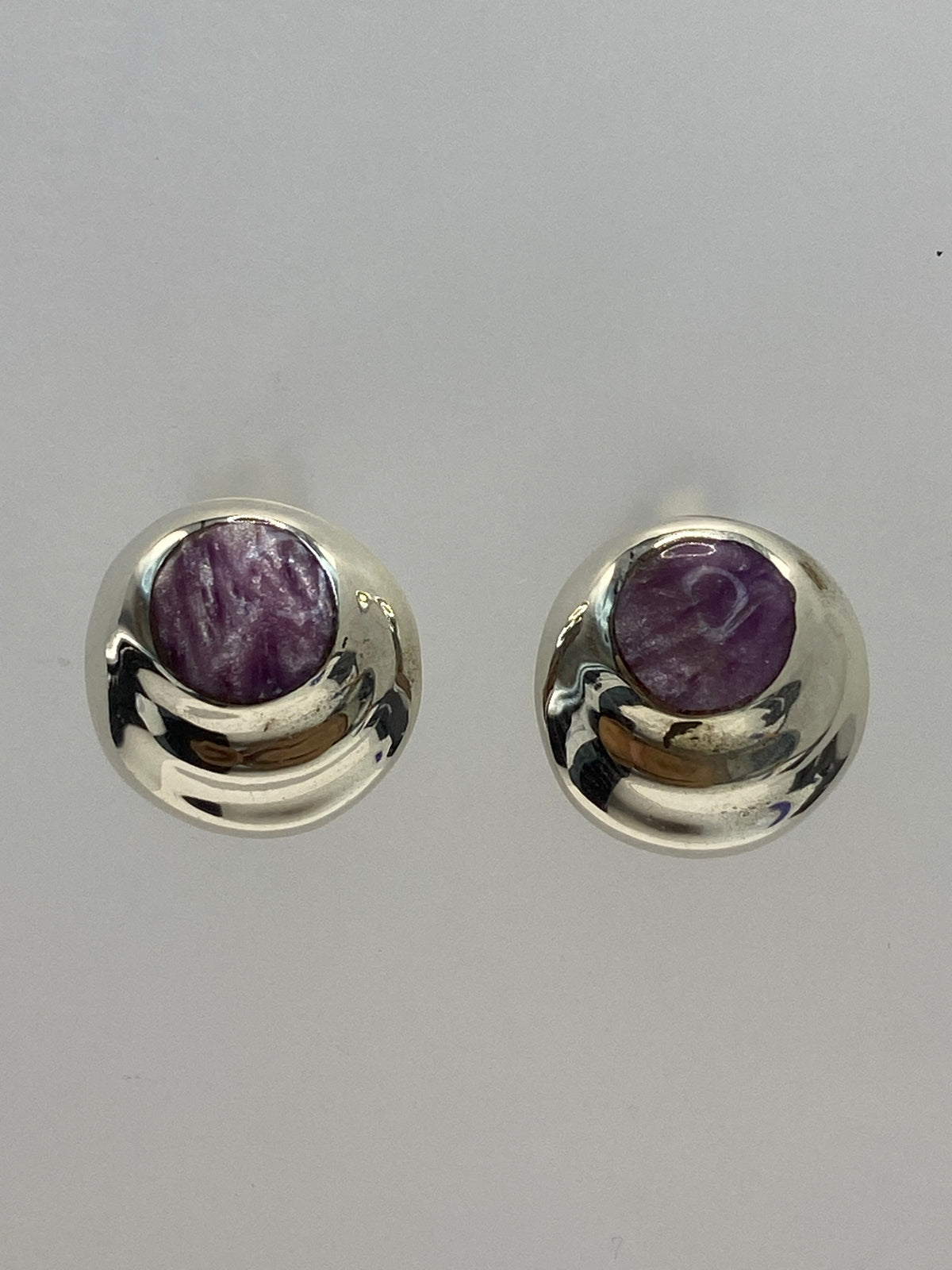 Par de aretes de plata 925 con piedra morada engastada, colgando sobre fondo blanco