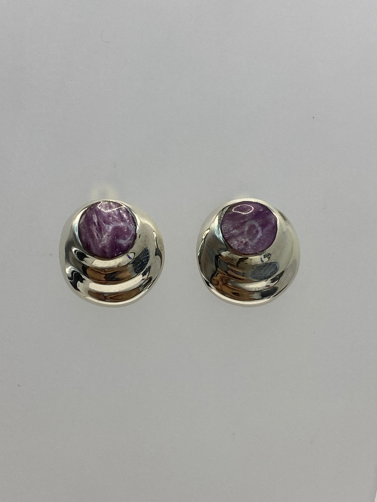 Detalle frontal de los aretes mostrando la incrustación de la piedra morada en la plata