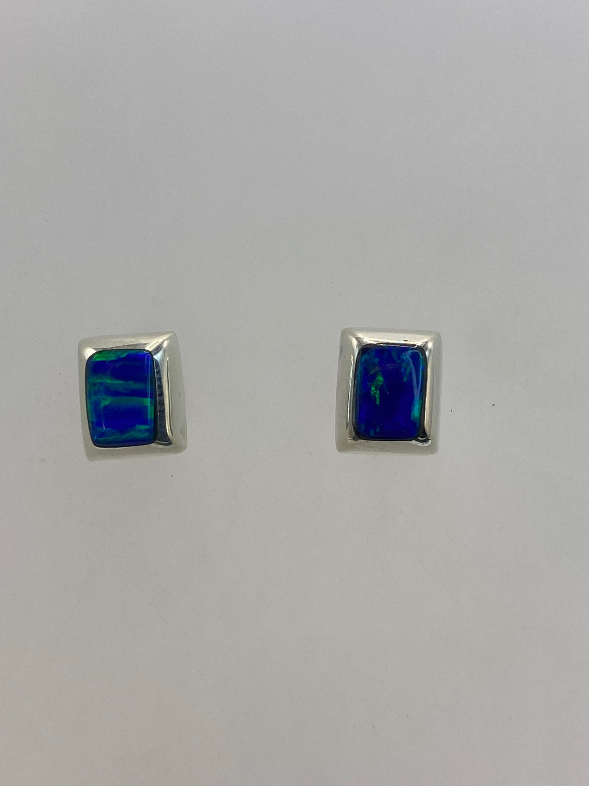 Par de aretes de plata con ópalo de fuego azul cielo engastado, sobre fondo blanco