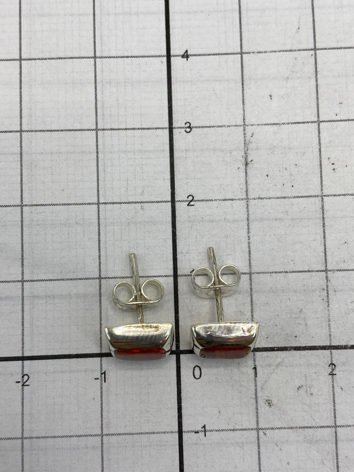 Aretes sobre fondo blanco mostrando el cierre de tuerca y la escala de tamaño (1.4 cm)