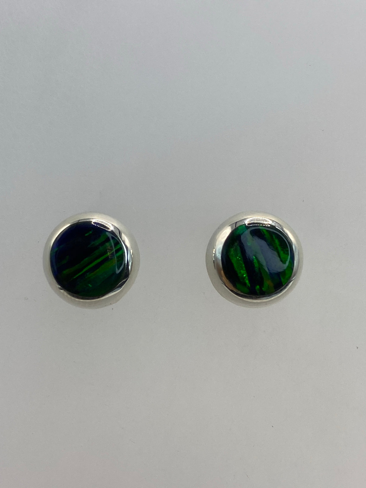 Par de aretes de plata con ópalo de fuego verde, frente a cara blanca