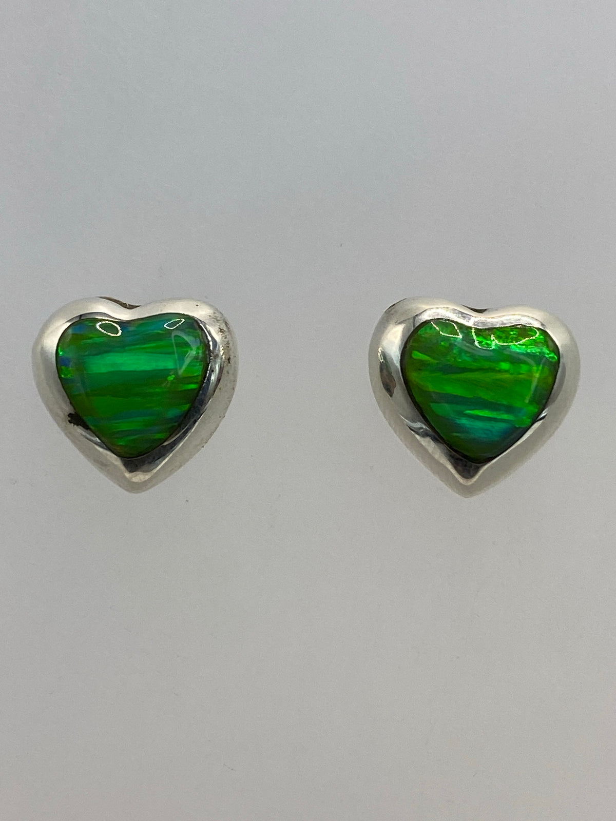 Aretes ópalo de fuego sobre fondo blanco mostrando el brillo verde limón