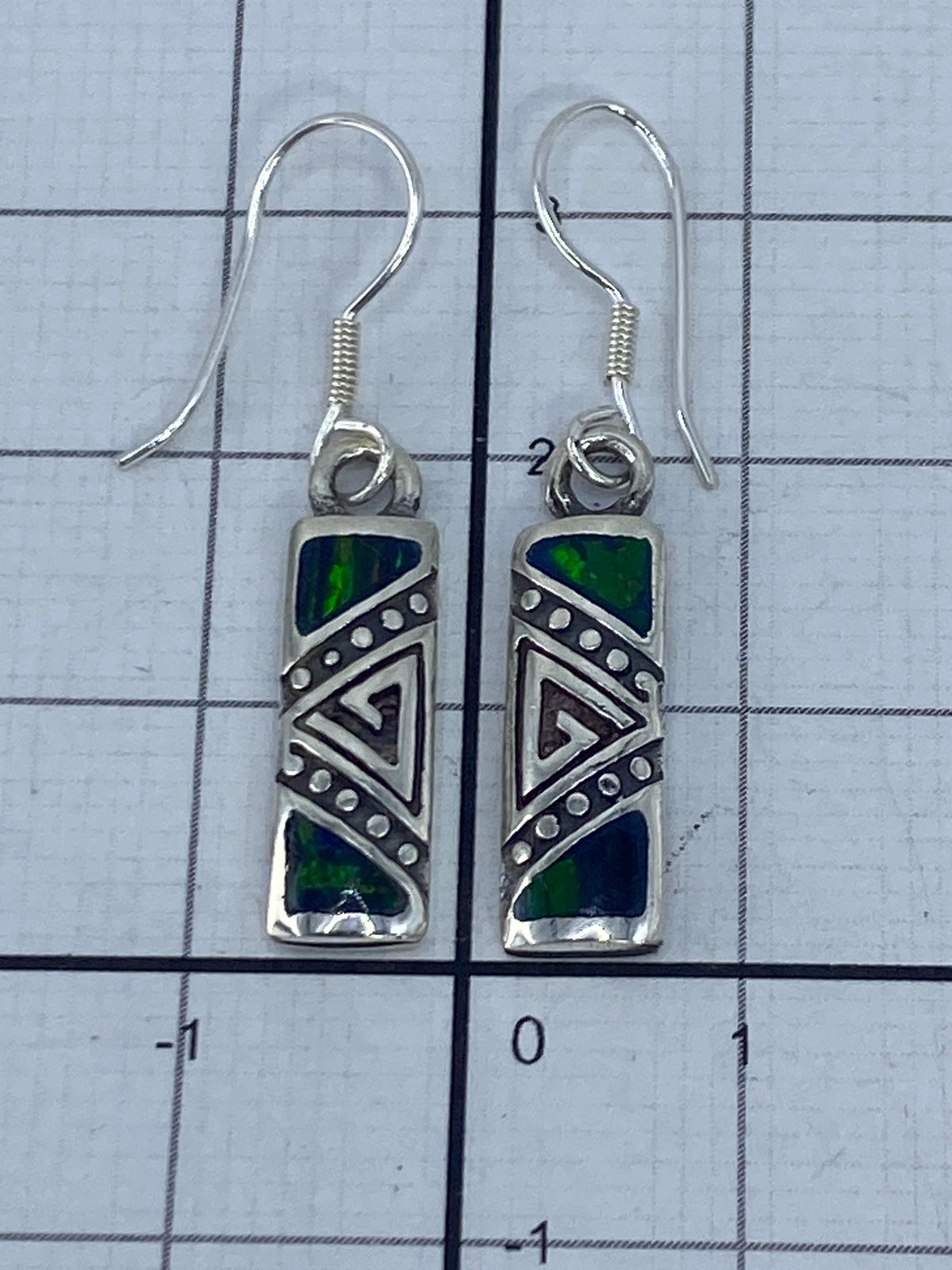 Dos aretes sobre fondo blanco con luz natural, ópalo de fuego verde iridiscente en plata 950