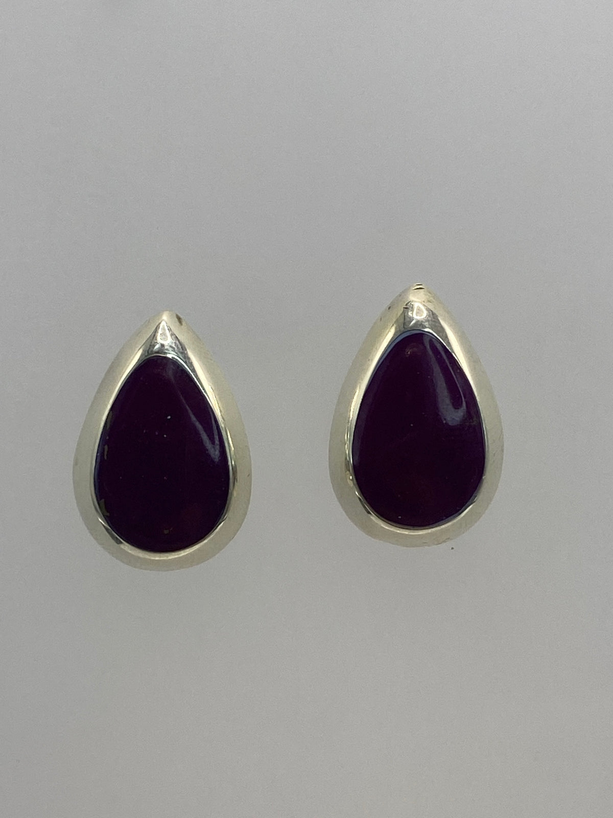 Aretes de plata 925 con piedra morada engastada, vistos de frente sobre fondo blanco