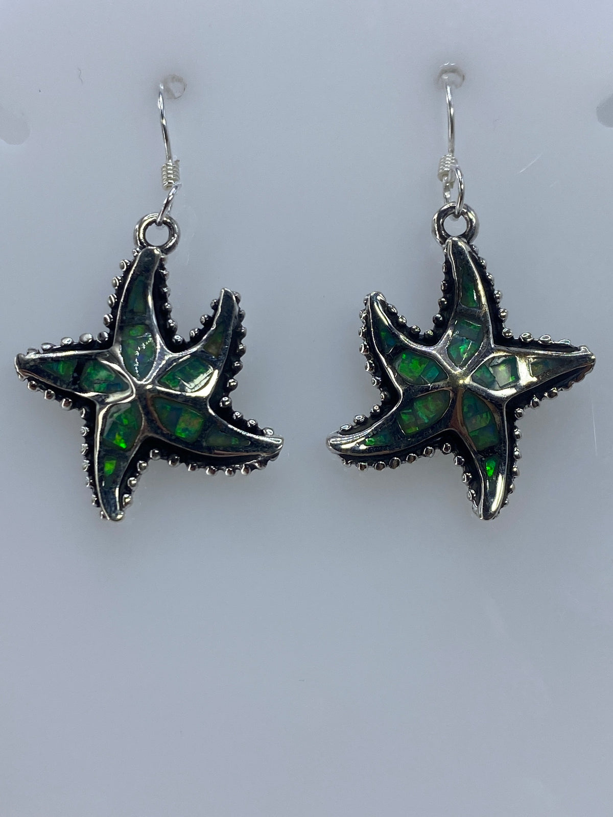 Aretes de ópalo de fuego mostrando el brillo iridiscente azul en luz natural