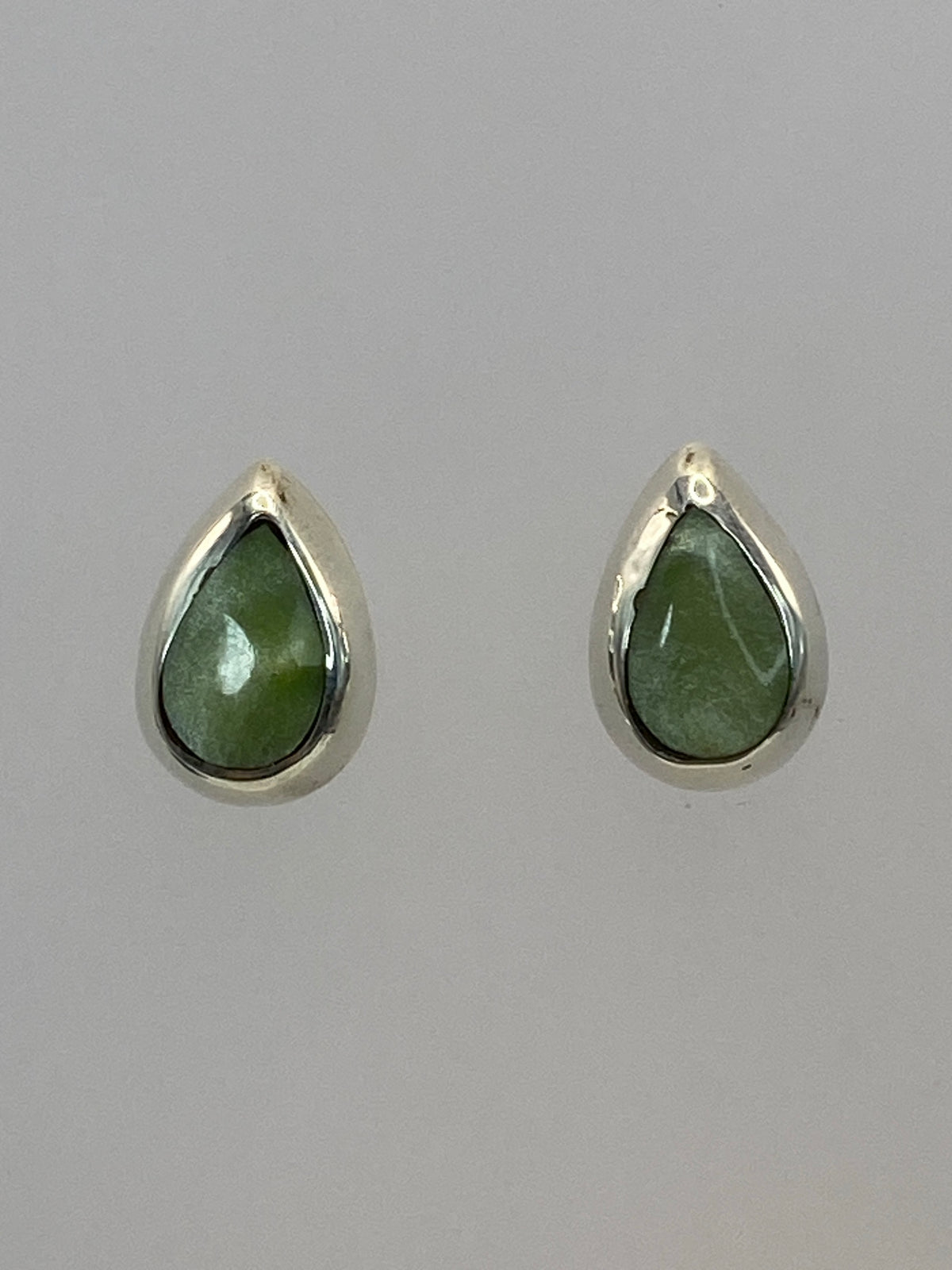 Par de aretes de plata con piedra verde engastada, forma de gota, sobre fondo blanco