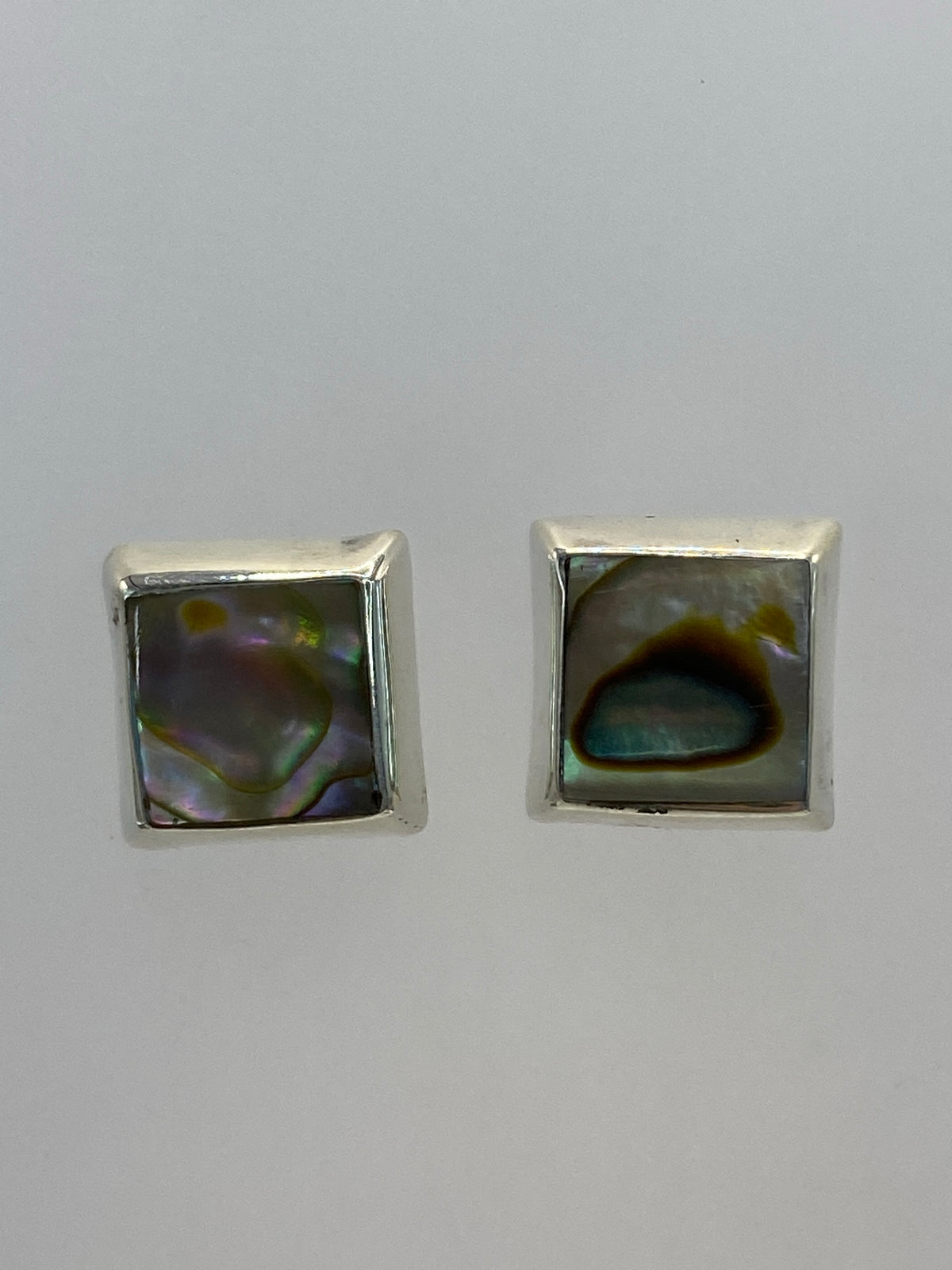 Par de aretes de plata cuadrados con piedra multicolor, posados en la palma de la mano