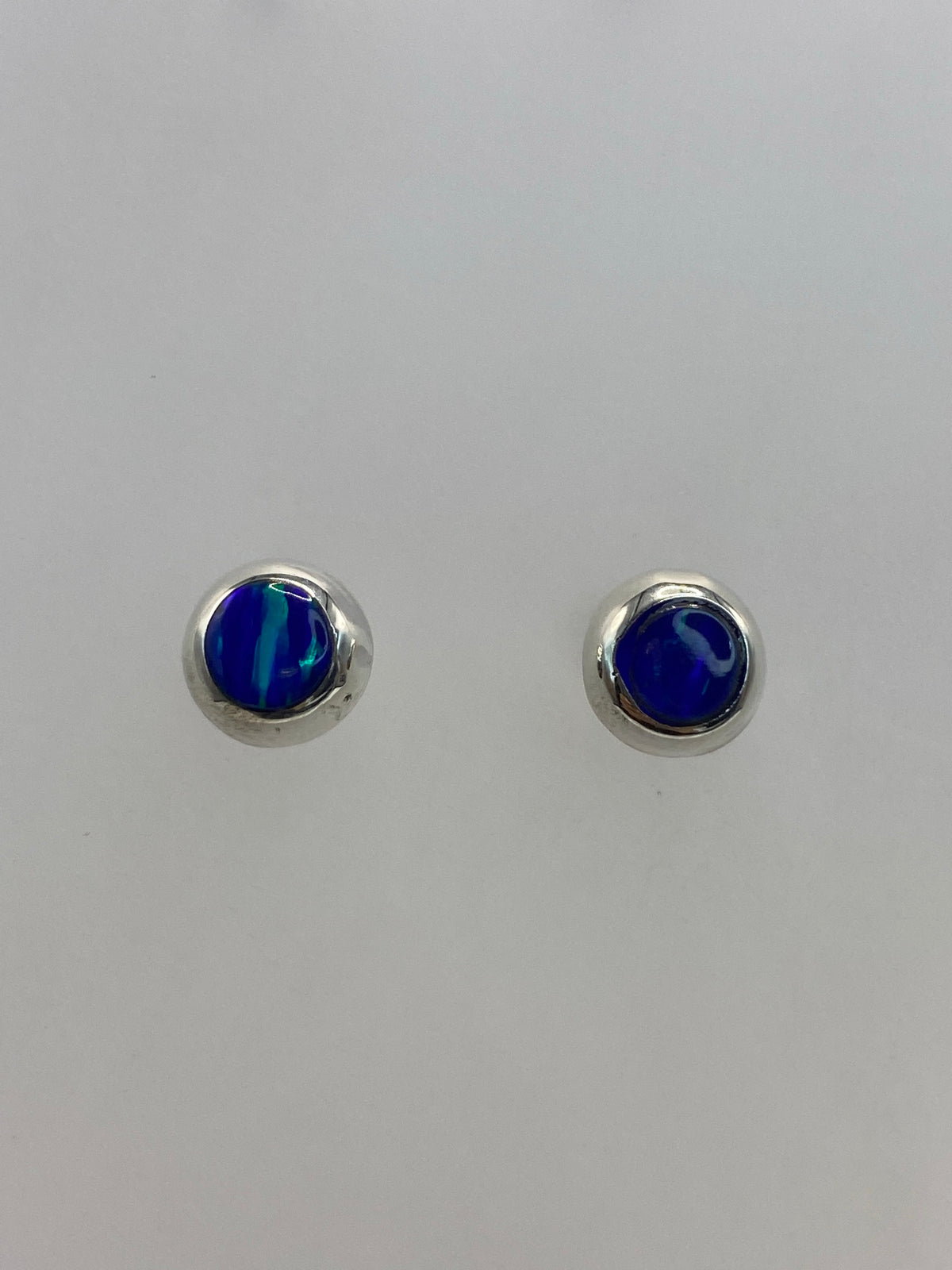 Par de aretes de plata 925 con ópalo de fuego azul, postes con mariposa, vista frontal sobre fondo blanco
