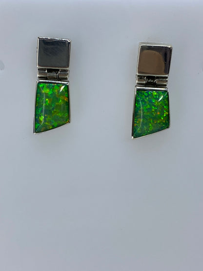 Par de aretes de plata con ópalo de fuego verde capturando luz natural, colgando contra fondo gris