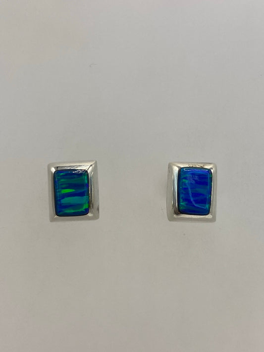 Par de aretes de plata con ópalo de fuego azul en la mano, mostrando el reflejo iridiscente
